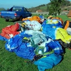Mehrere Gleitschirme liegen auf der Wiese mit einem blauen Auto im Hintergrund