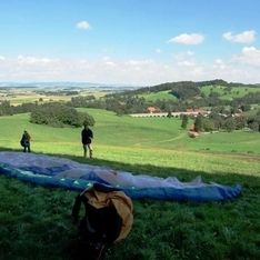 Ein Paragleitschirm liegt ausgebreitet auf der Wiese vor einem Mann