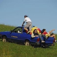 Unser blaues Auto der Flugschule Kilb Freewind mit Personen und Gleitschirmen auf der Ladefläche auf einer Wiese