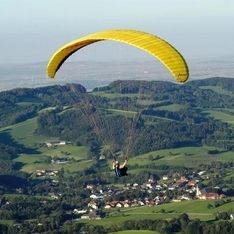 Ein Paragleiter fliegt mit gelbem Schirm und Natur im Hintergrund