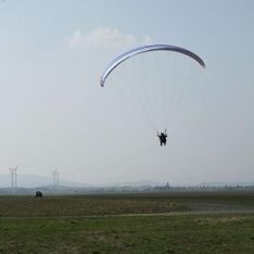 Ein Paragleiter auf einer Wiese vor blauem Himmel im Hintergrund
