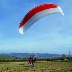 Ein Paragleiter auf einer Wiese vor blauem Himmel im Hintergrund