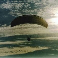 Ein Paragleiter fliegt in der Luft vor blauem Himmel im Hintergrund