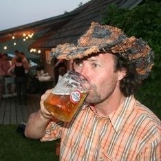 Eine Person mit Hut trinkt ein Glas Bier vor der Hütte