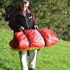 Eine Person mit einem zusammengepackten Gleitschirm in der Hand auf einer Wiese