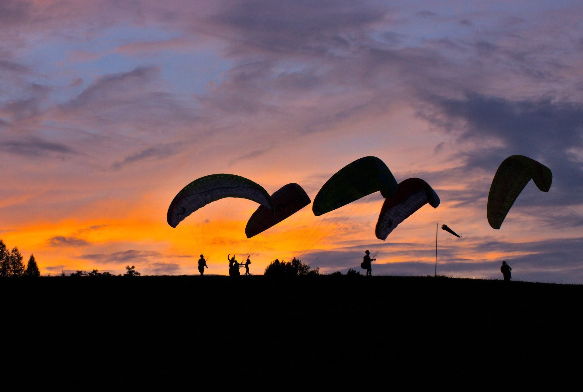 Mehrere Paragleiter auf einem Berg mit Sonnenuntergang im Hintergrund